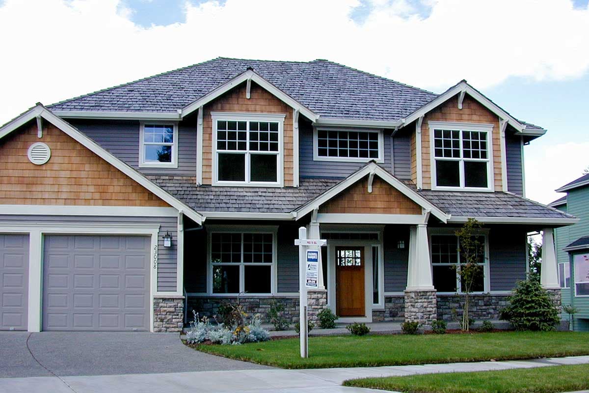 House plan exterior: two-story home with gabled dormers, cedar shingle siding, stone accents, and a covered entry porch.