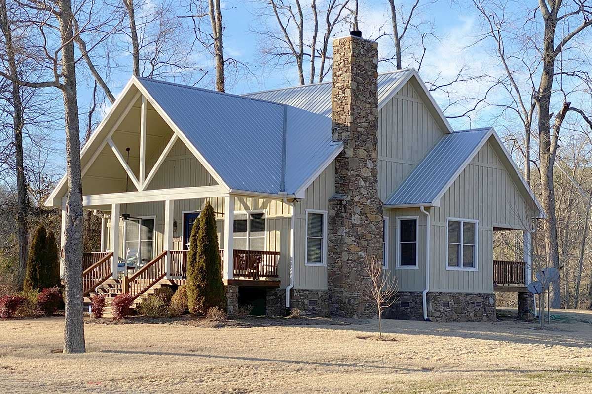 House plan exterior. One-story Modern Farmhouse with a gabled roof, stone chimney, and covered front porch with a railing.