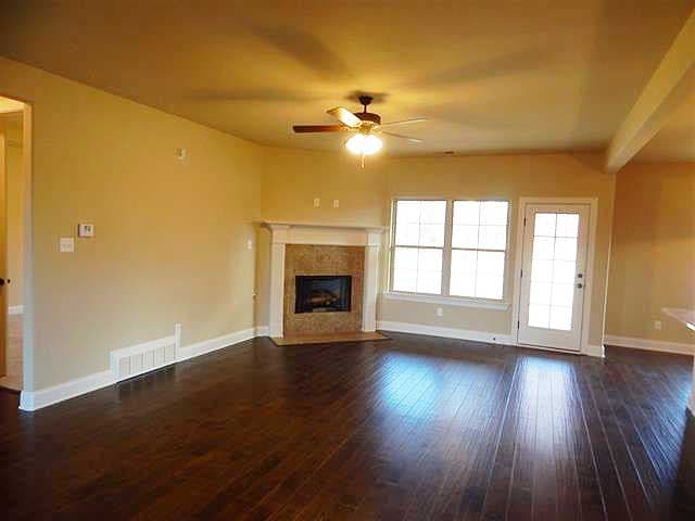 Great room with fireplace, ceiling fan, door to exterior, and windows.