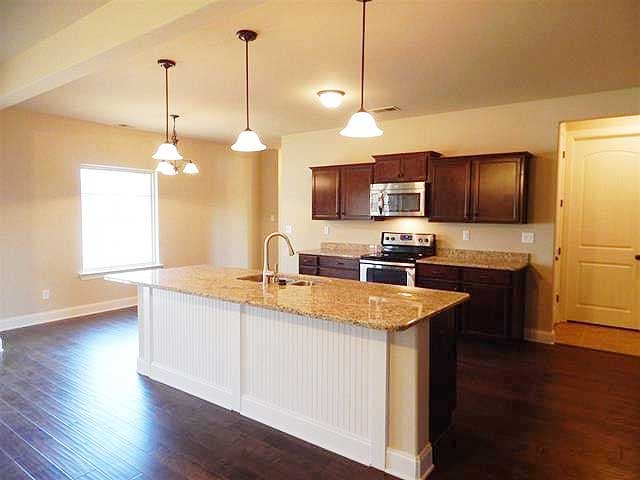 Kitchen with granite island, dark wood cabinets, stainless steel appliances, and pendant lighting.