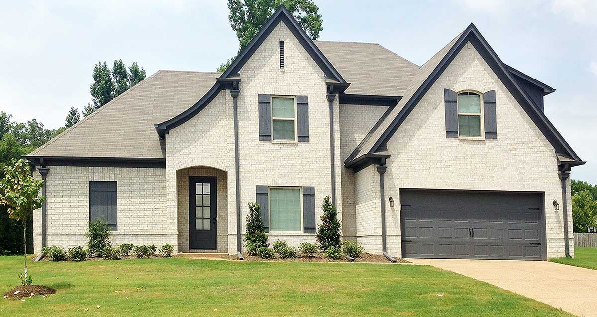 Two-story house plan exterior with white brick, dark gables, arched entryway, and attached garage.