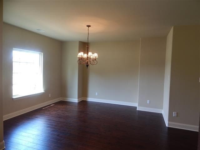 Interior view of a dining room with dark wood floors, a large window, and a traditional chandelier.