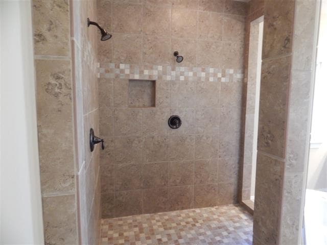 Tiled shower with dual showerheads, built-in niche, and mosaic tile accent band. Floor features mosaic tile.