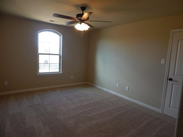Interior view of an unfurnished room with carpet, a ceiling fan, and an arched window.