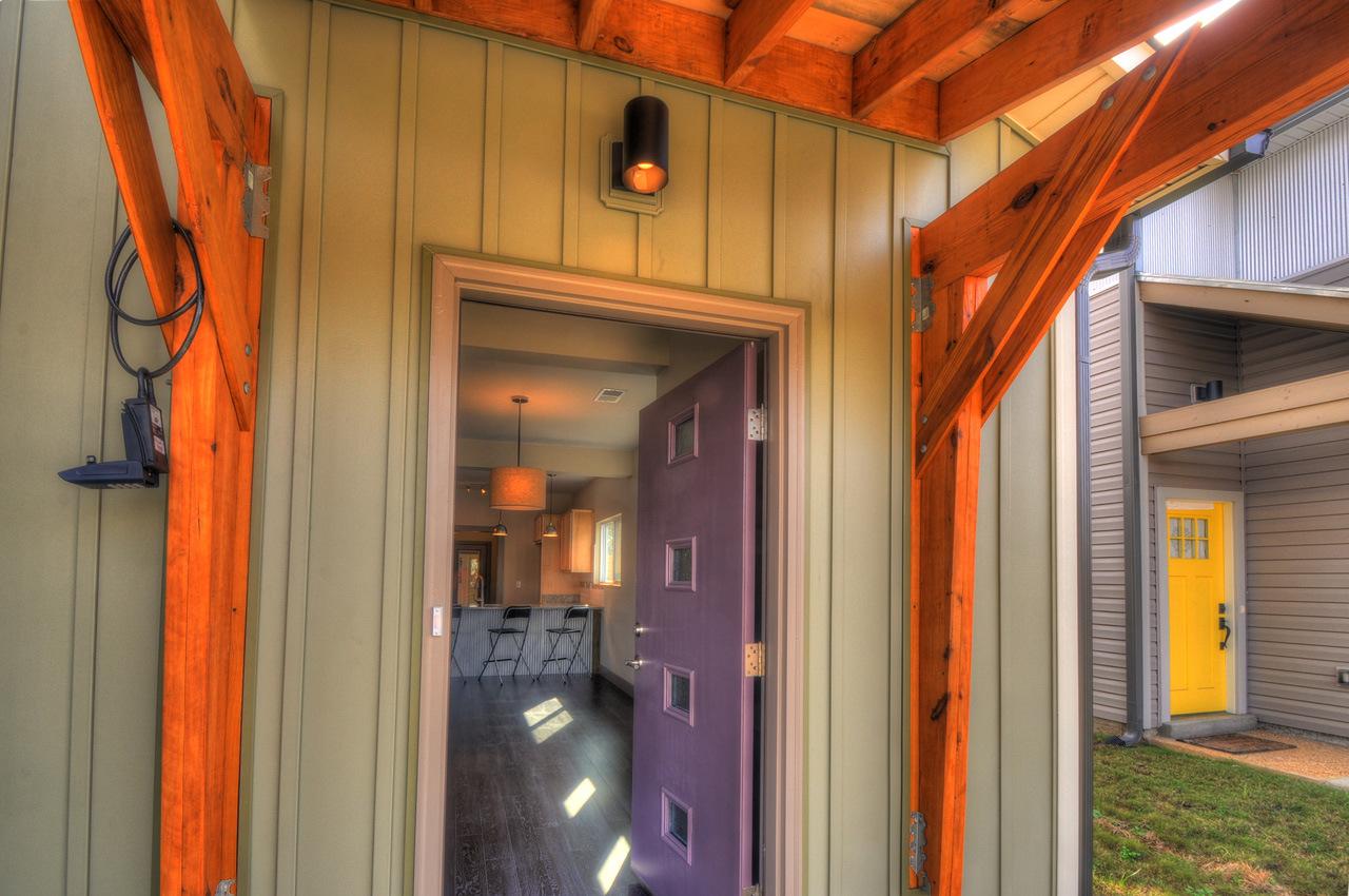 Exterior house plan: entry porch with green siding, exposed wooden beams, and purple front door opening to interior kitchen with island.