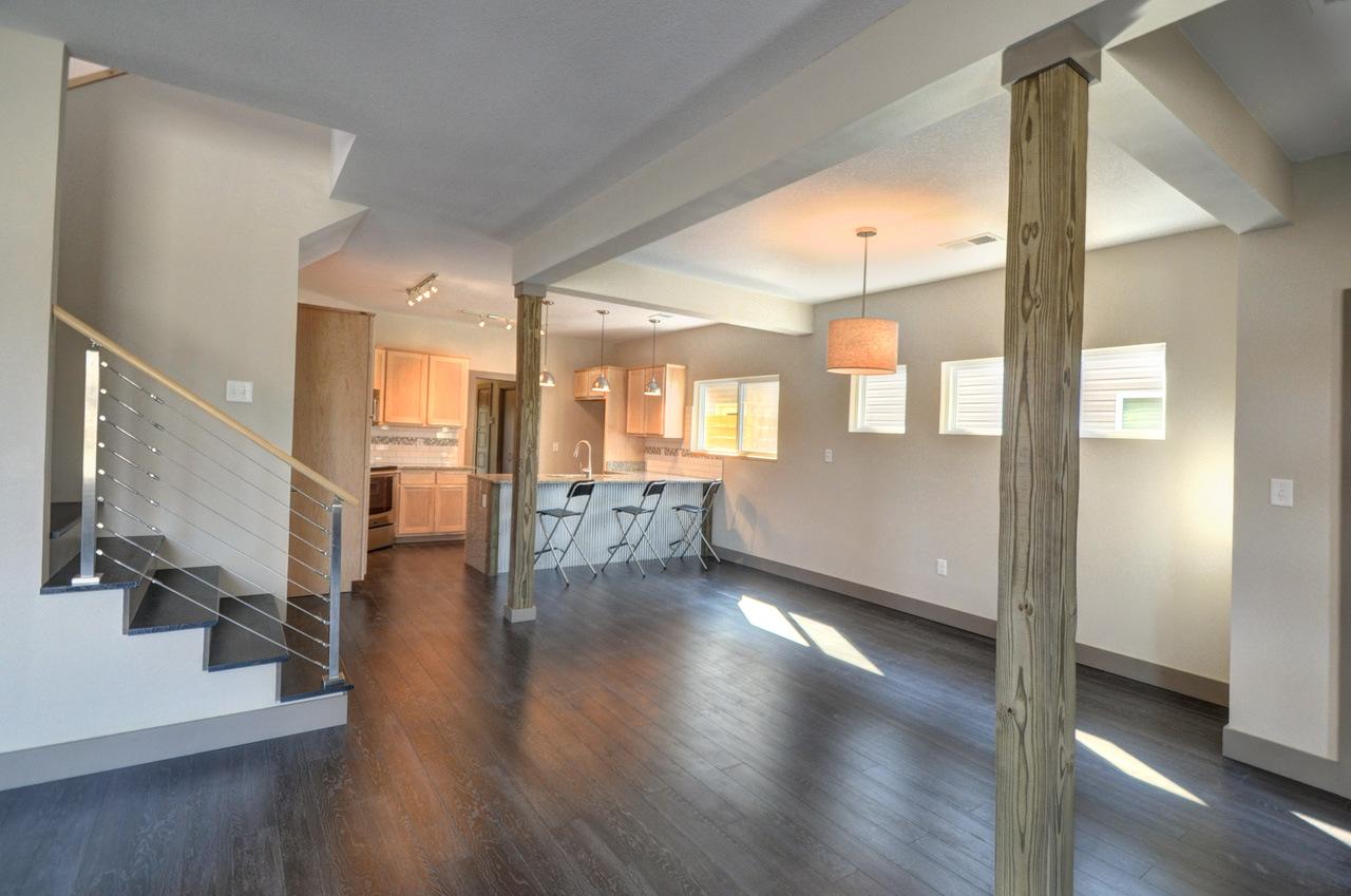Interior view of an open-concept living area with a kitchen island, bar seating, and a staircase with cable railings.
