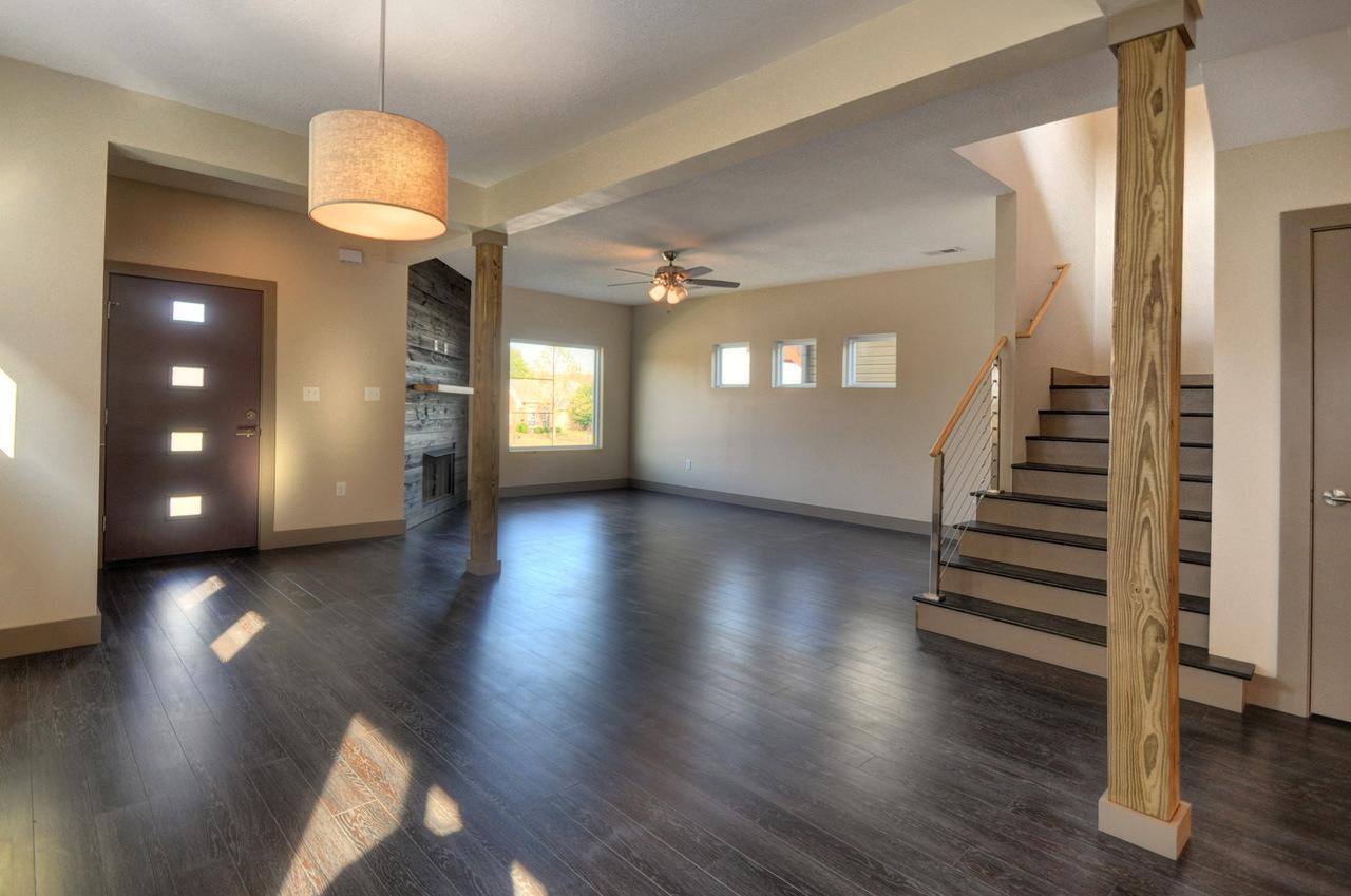 Interior view of a house plan showing an open living space with a modern door, stacked stone fireplace, and staircase.