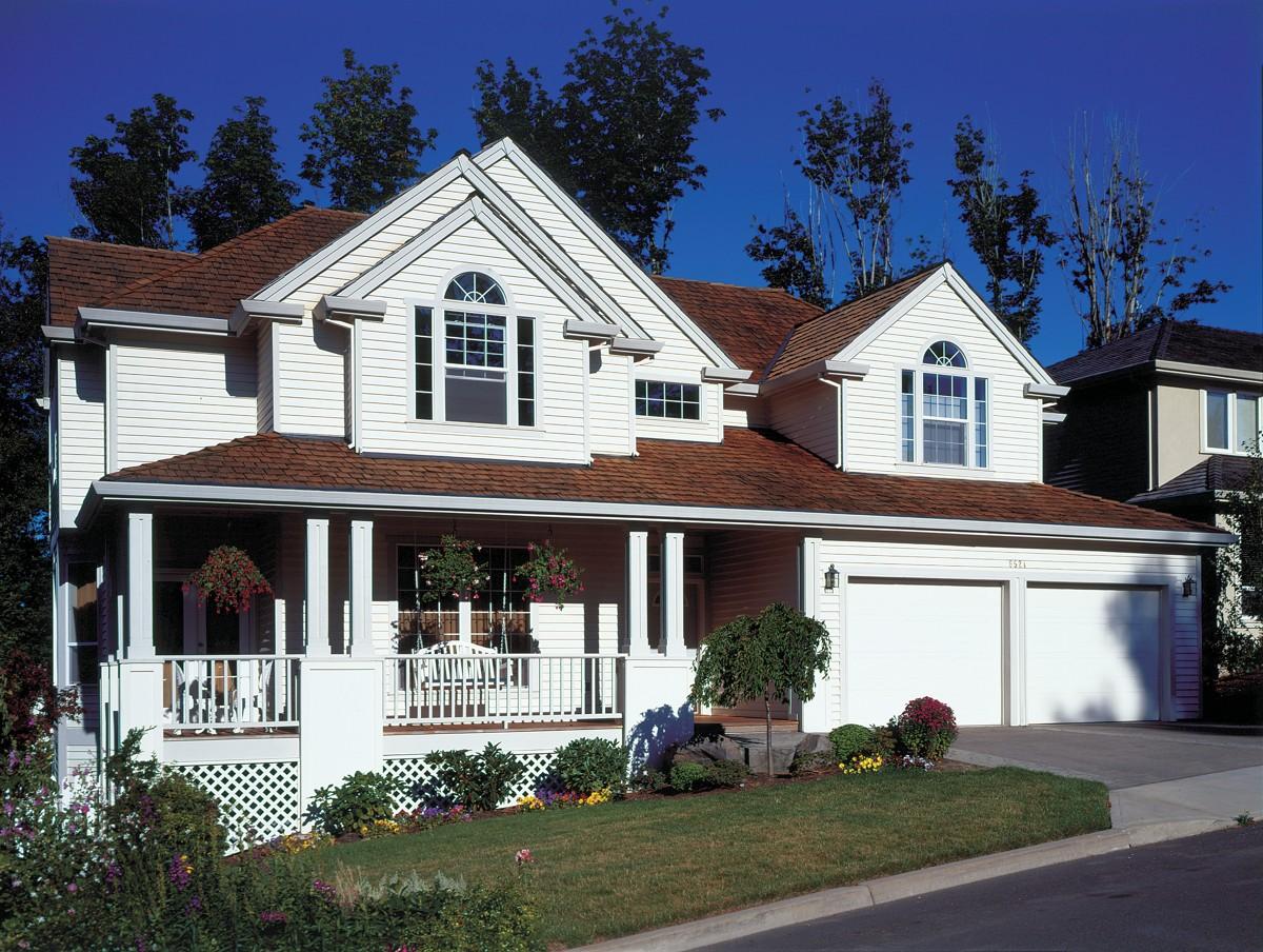 Two-story house plan exterior with a wrap-around porch, gabled dormers, arched windows, and a three-car garage.