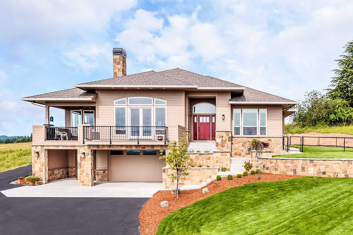 House plan exterior. Two-story with stone facade accents, covered balcony, and a multi-pane window design. Garage is beneath the balcony.