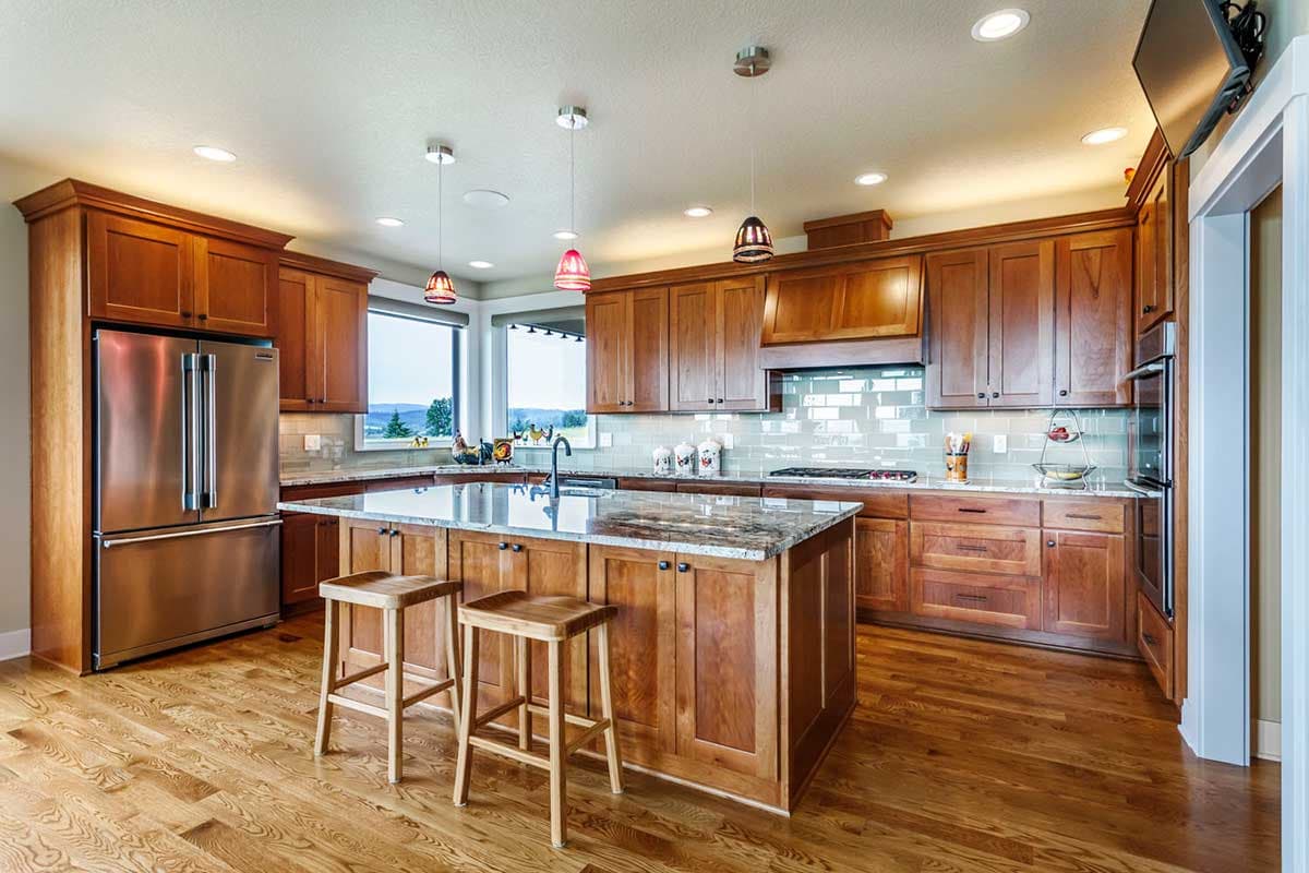 Kitchen with central island, stainless steel refrigerator, granite countertops, wood cabinetry, and a bay window.