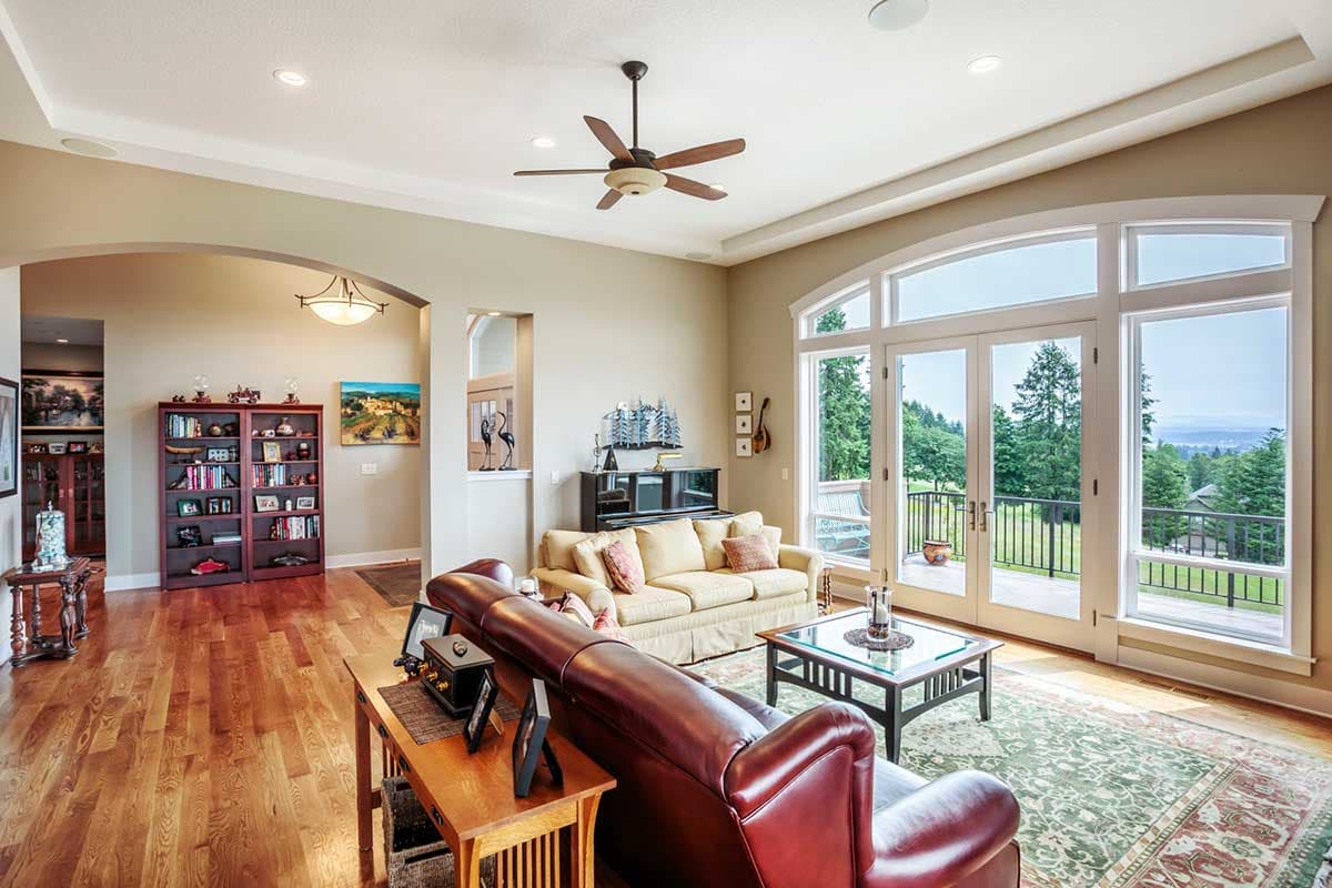 Living room with vaulted ceiling, fireplace, and large windows overlooking a landscaped yard.