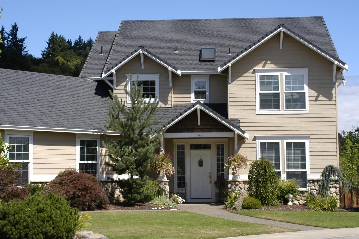 House plan exterior: Two-story, beige siding, gabled roof with dormers, covered entry porch with stone pillars.