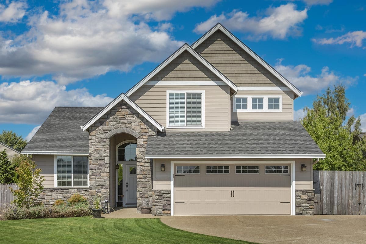 House plan exterior: Two-story home with stone accents, prominent gabled dormer, arched entryway, and a wide garage.
