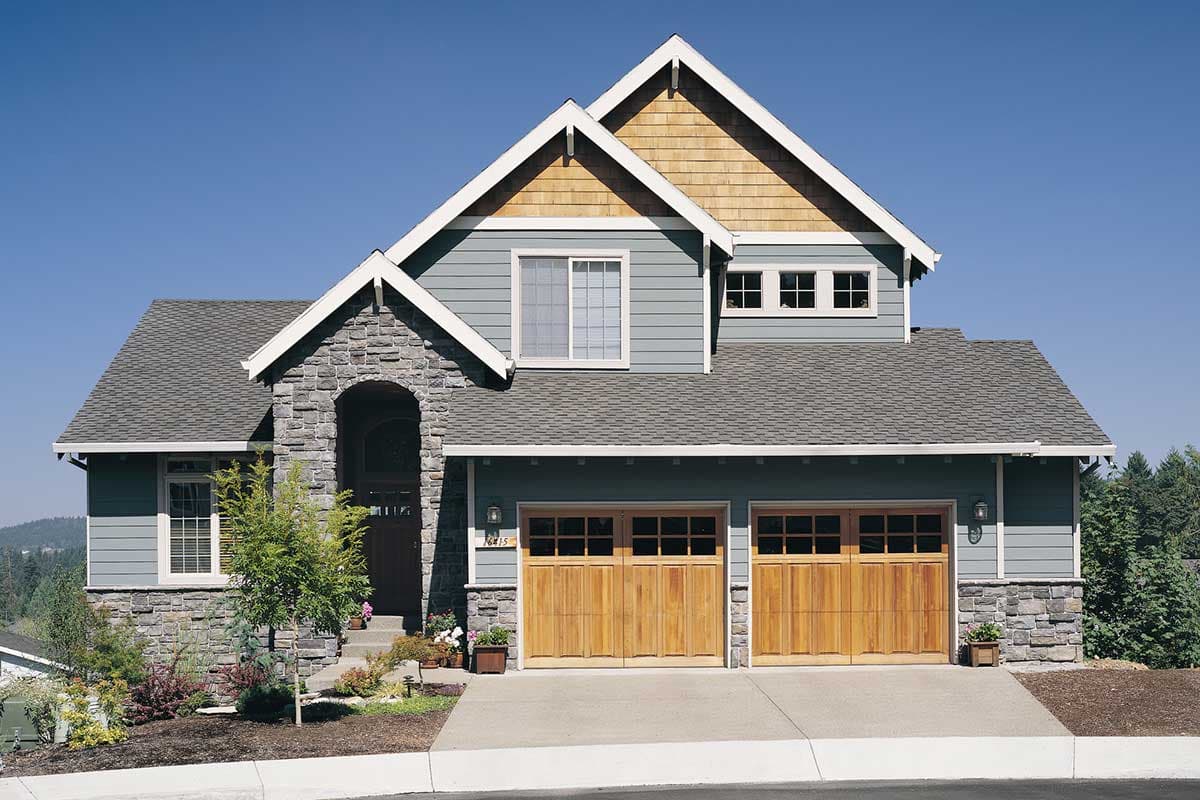 House plan exterior: Two-story home with stone accents, arched entryway, wood garage doors, and multiple gables.