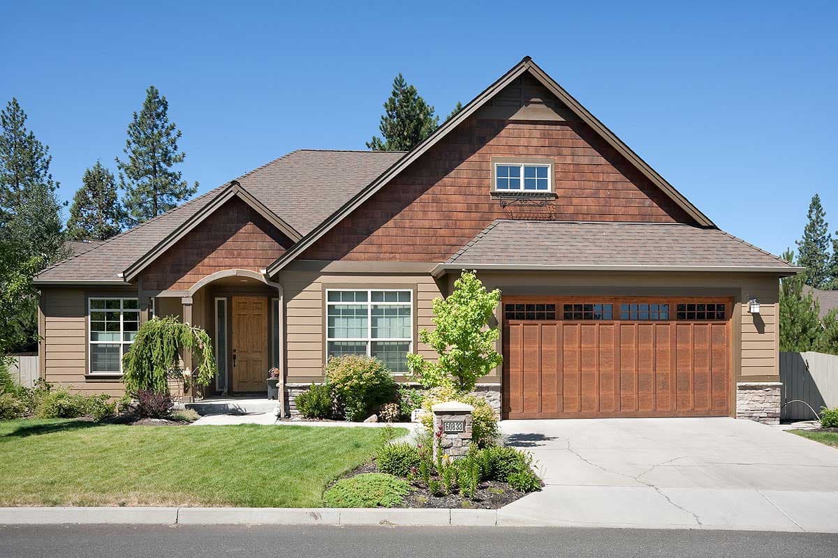 House plan exterior of a one-story home with wood siding, stone accents, arched entry, and a large wood garage door.