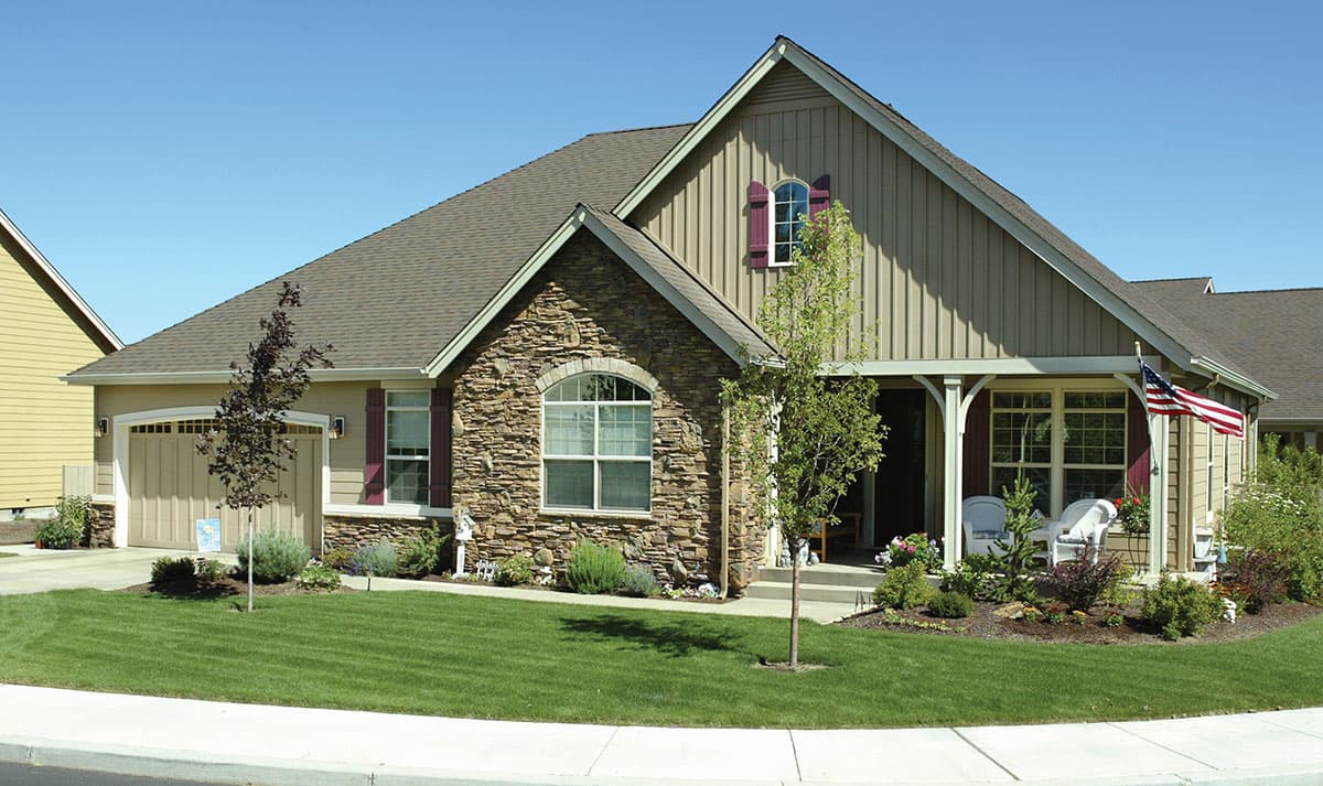 House plan exterior with stone facade, arched window, dormer, covered porch with columns, and attached garage.