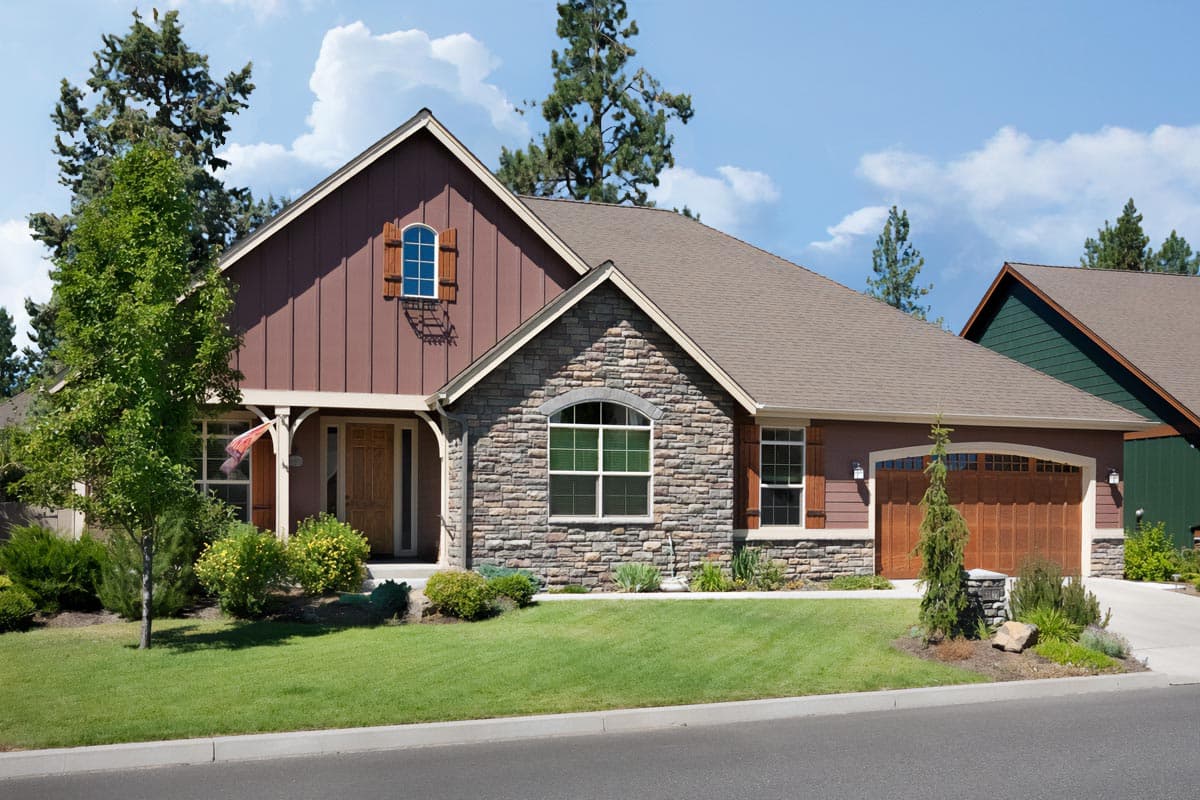 House plan exterior: Single-story Modern Farmhouse with stone facade, wood siding, arched dormer, and attached two-car garage.