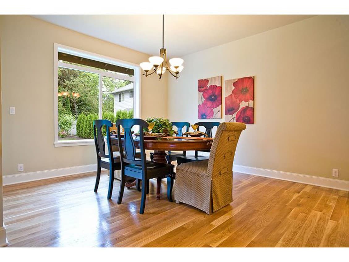 Dining room with round table, dark wood chairs, and a large window overlooking greenery.