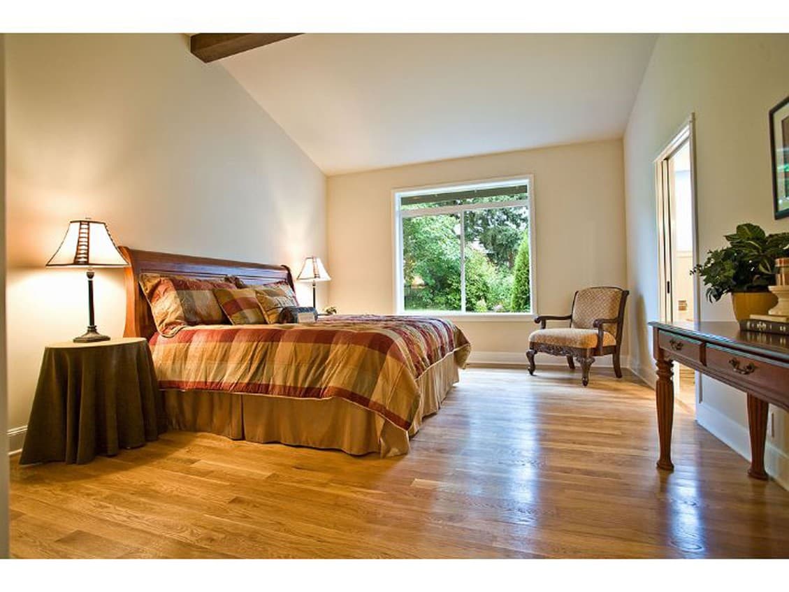 Bedroom with vaulted ceiling, wood beam accent, and large picture window overlooking greenery.
