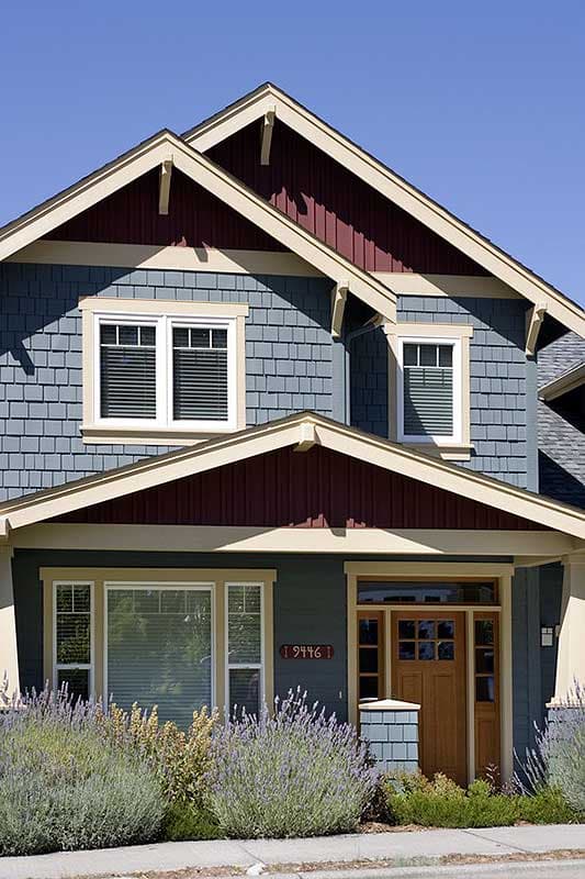 Craftsman style house plan exterior with blue shingle siding, burgundy gables, exposed rafter tails, and wood door.