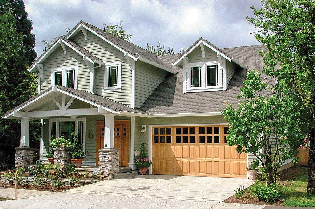 House plan exterior: two-story home with wide front porch, stone base pillars, dormers, and a wooden garage door.