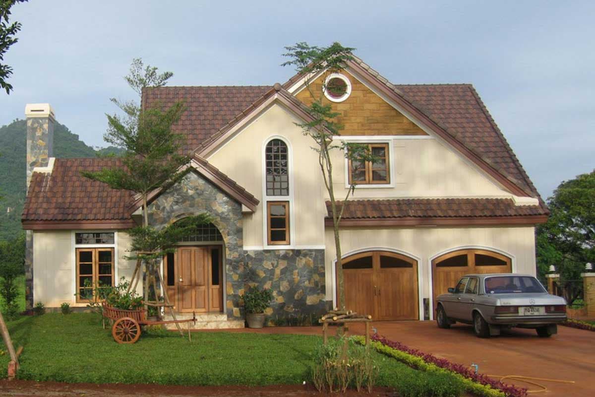 House plan exterior with stone-clad entry, arched windows, dual garage doors, and a prominent gable with circular dormer.