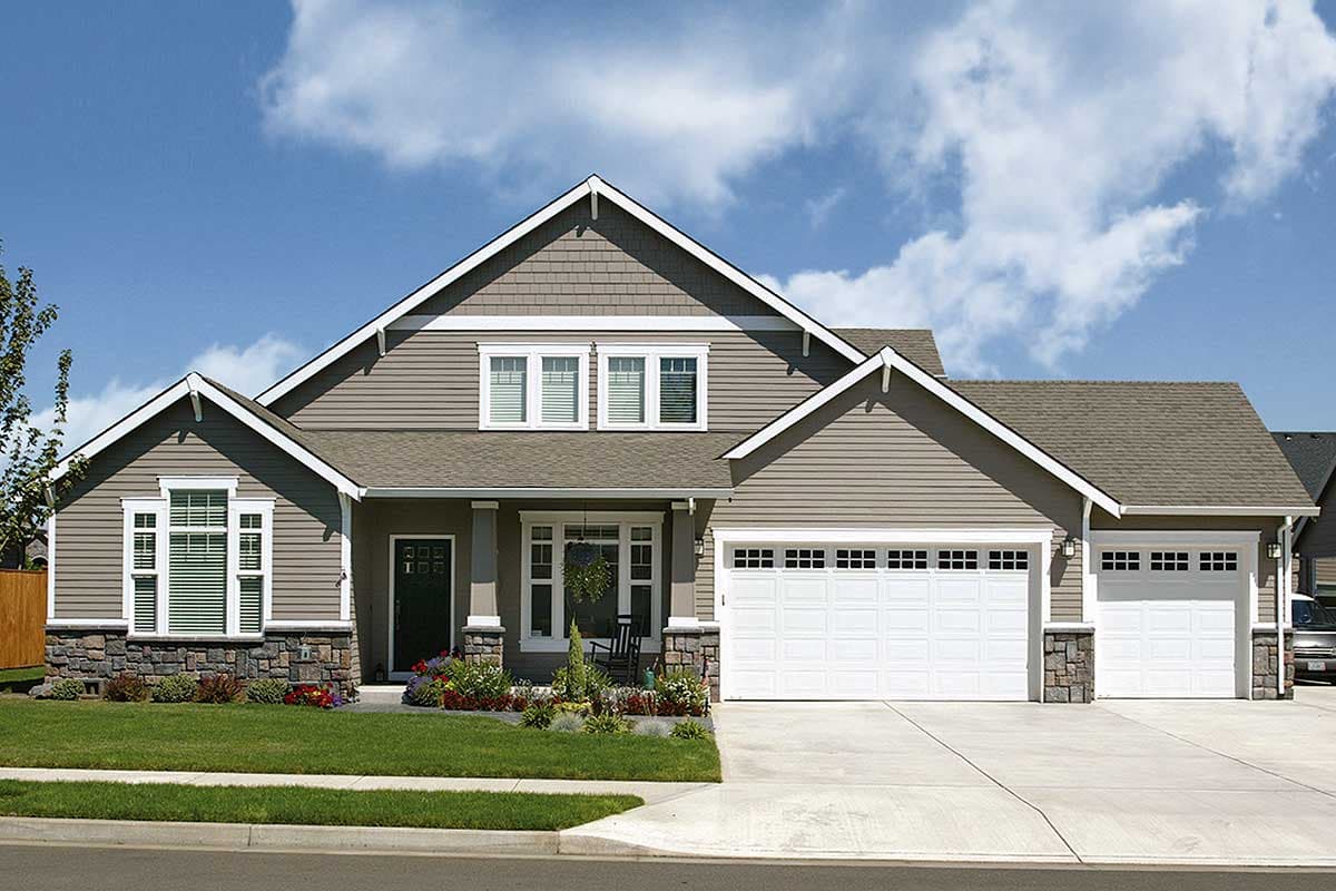House plan exterior: Two-story home with gabled dormers, stone accents, covered porch, and a three-car garage.