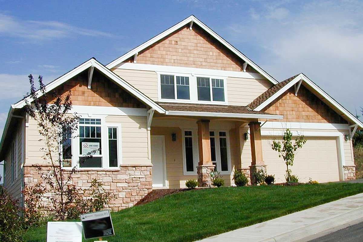 House plan exterior: Two-story home with stone base, wood shingle gables, covered porch with columns, and attached garage.