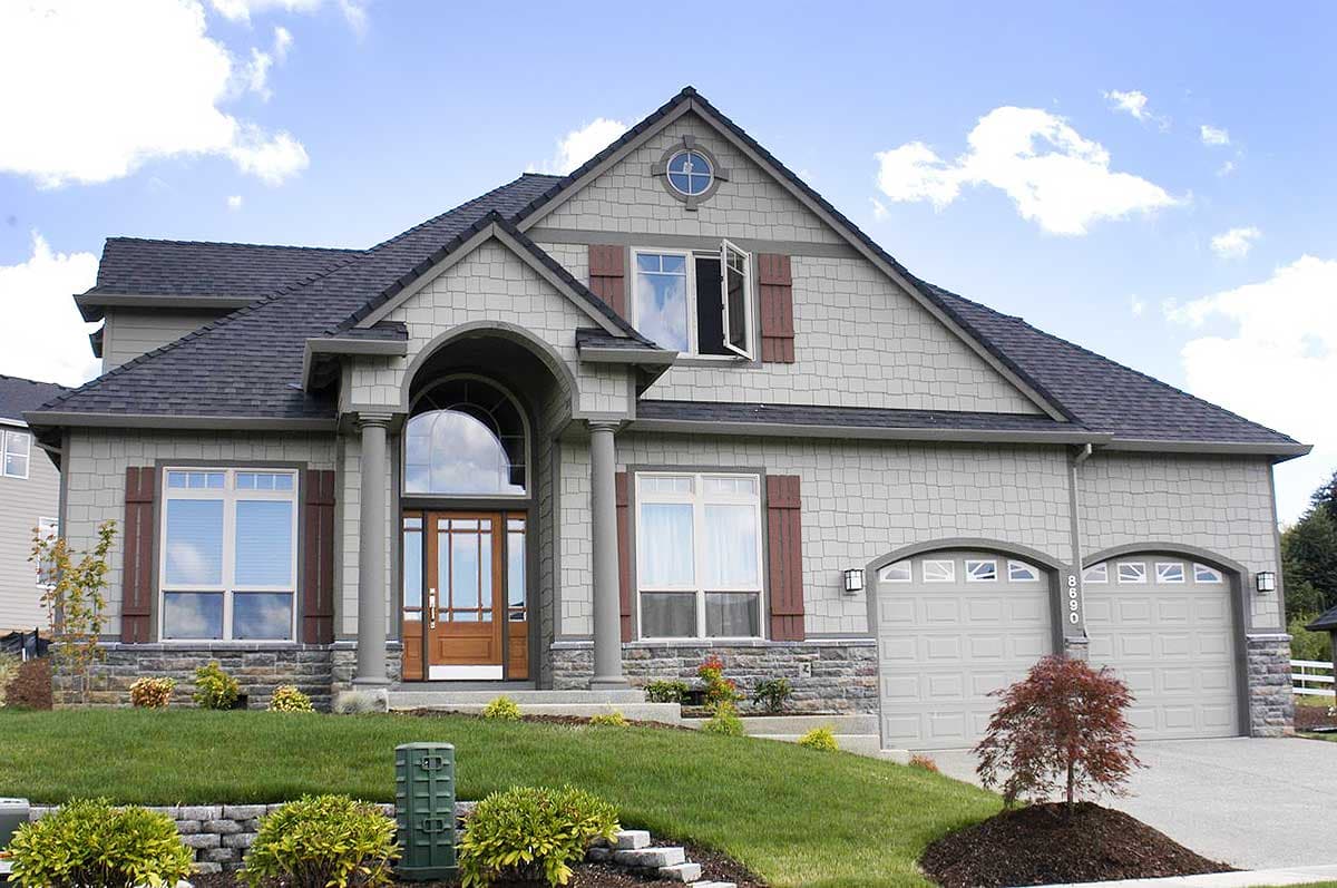 House plan exterior featuring a prominent arched entryway with columns, dual garage doors, and prominent gables.