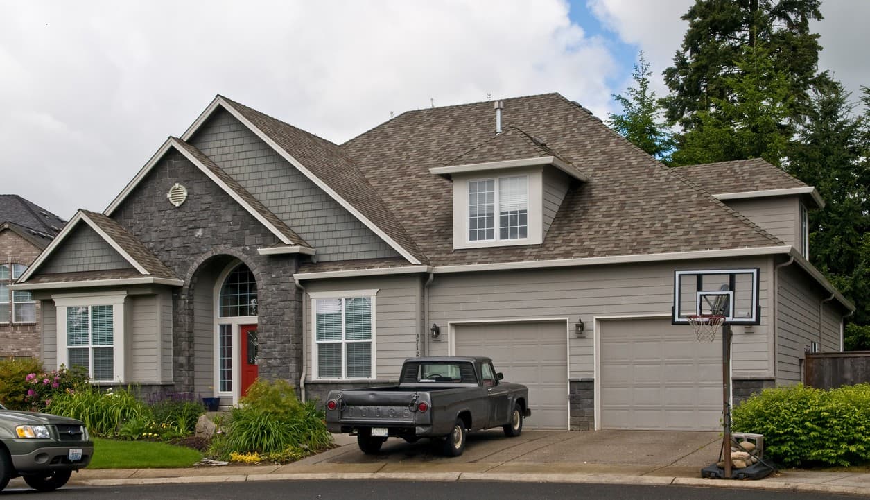 House plan exterior: Two-story home with hip roof, dormer, gabled entrance with stone accents, and a three-car garage.