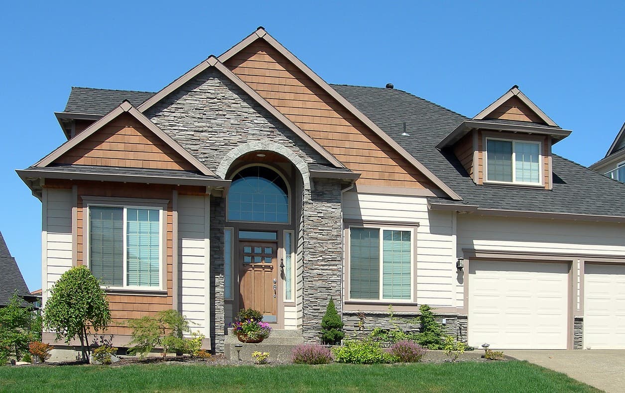 House plan exterior: Two-story home with stone and shingle accents, arched entryway, dormer, and attached three-car garage.