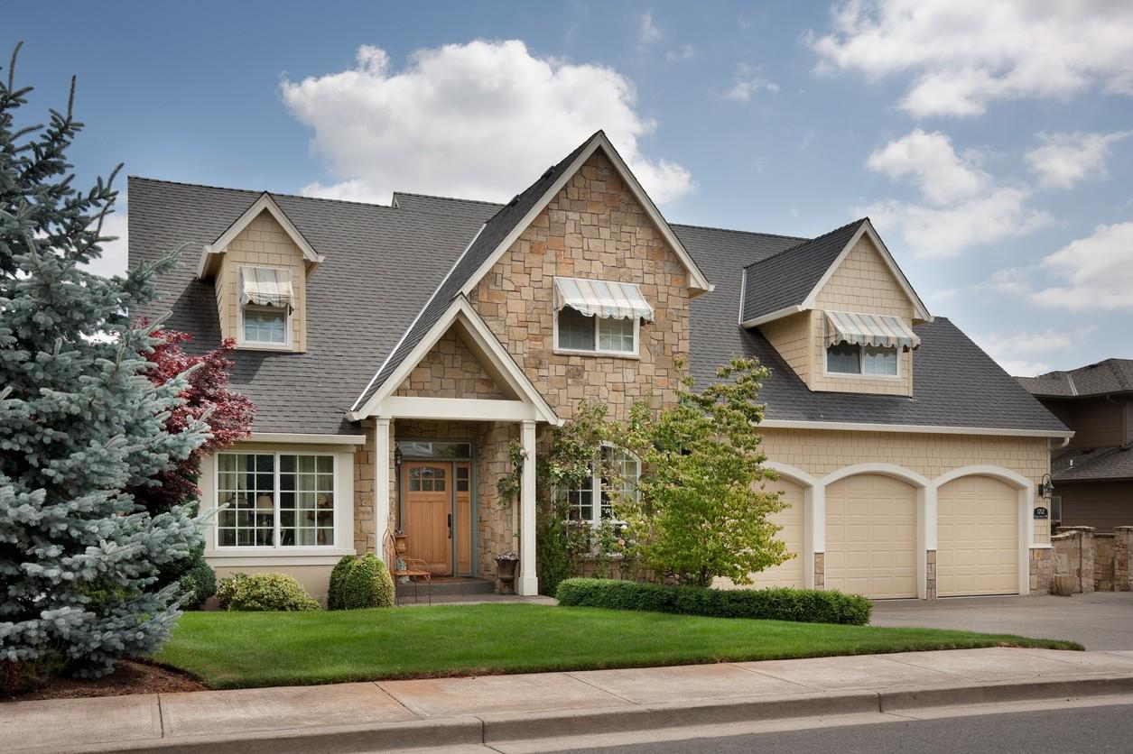 House plan exterior: Two-story home with stone and shingle siding, front-facing gables, dormer windows, and a three-car garage.