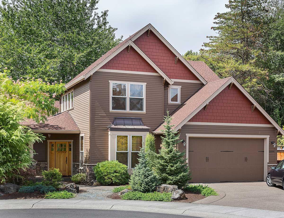 Two-story house plan exterior with red shingle gables, wood siding, covered porch, bay window, and attached two-car garage.