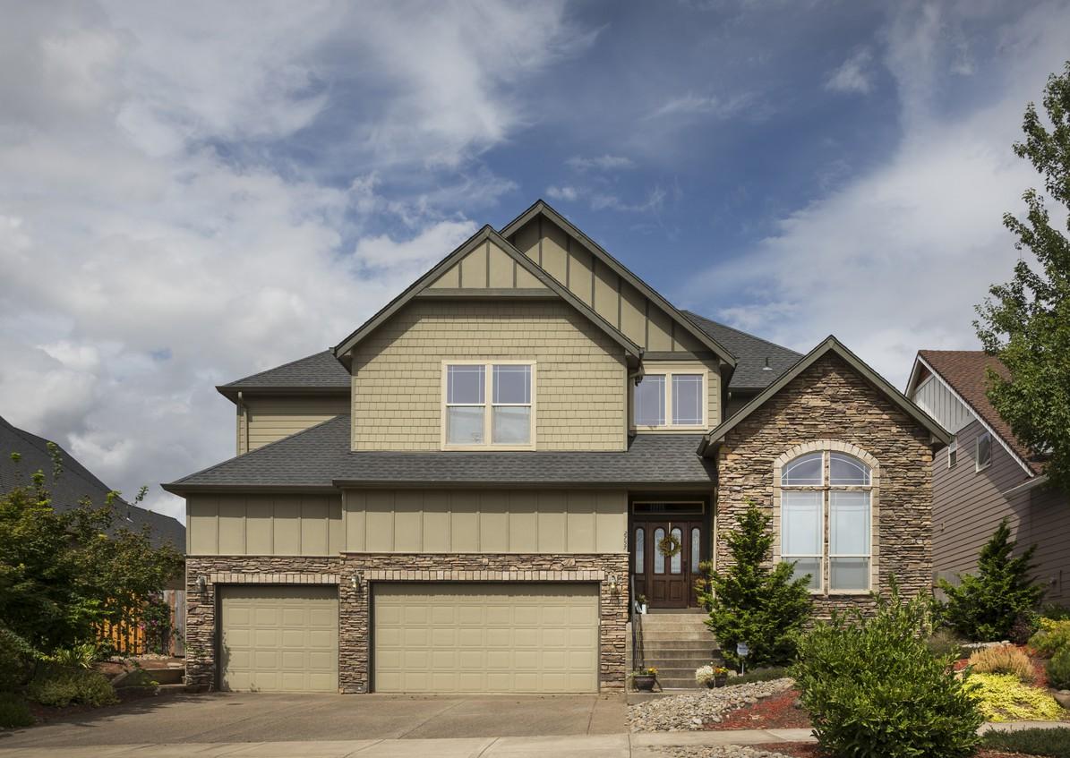 Two-story house plan exterior with three-car garage, stone accents, arched window, gables, and shingle siding.