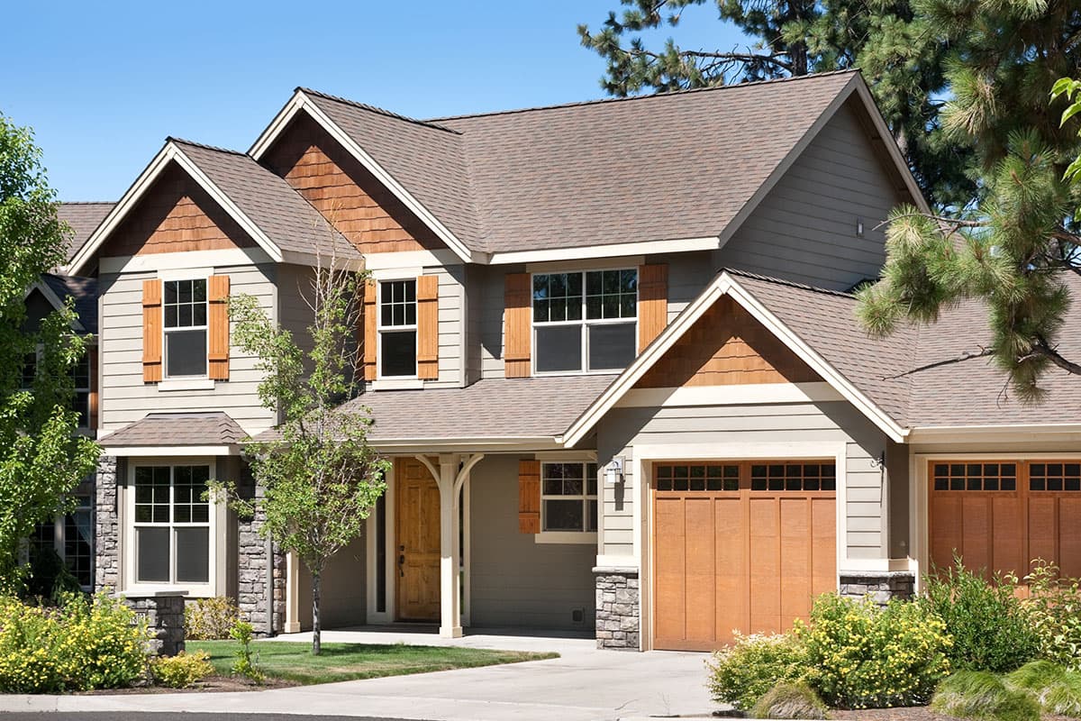 House plan exterior: two-story home with gabled rooflines, stone accents, wood shutters, and a double garage.