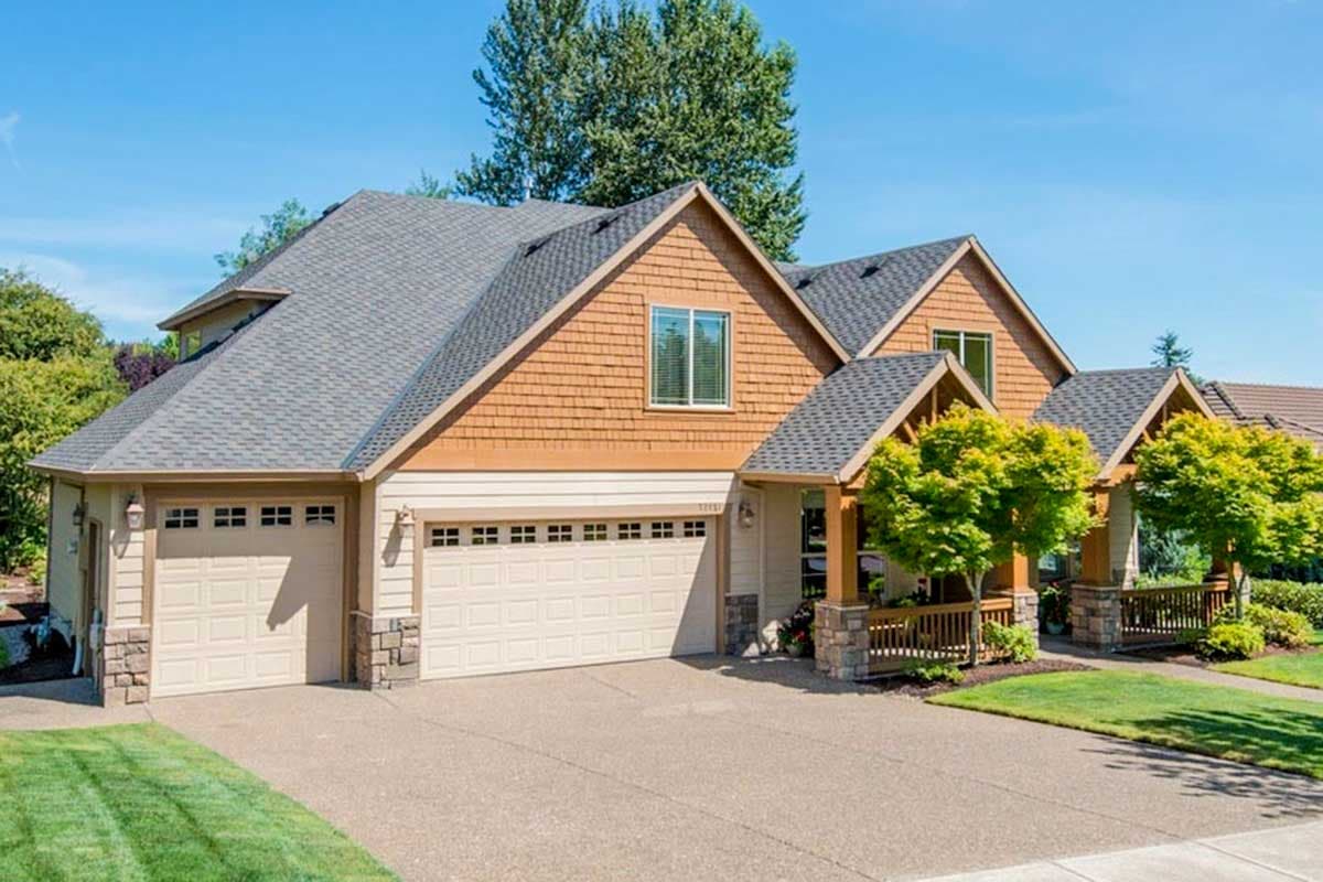 House plan exterior: Two-story home with wood shake siding, multiple gables, a covered front porch, and a three-car garage.
