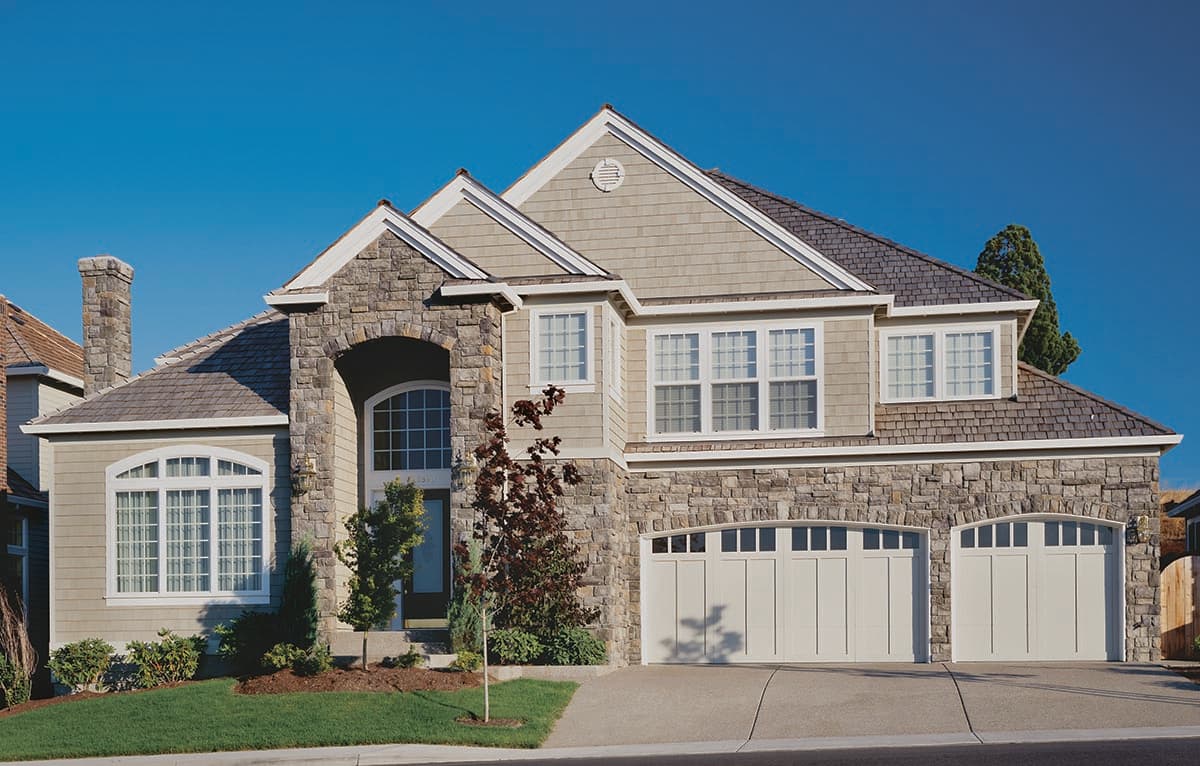 House plan exterior: Two-story home with stone accents, arched entryway, dormers, and a triple-bay garage with segmented top panels.