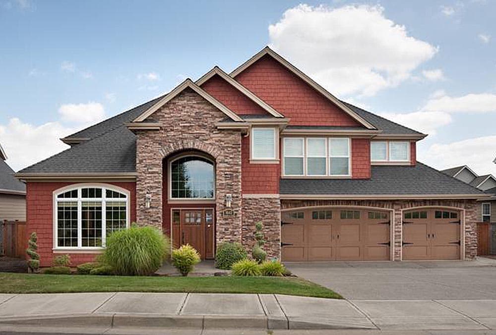 House plan exterior: Two-story home with stone accents, arched entryway, multiple gables, and a three-car garage.
