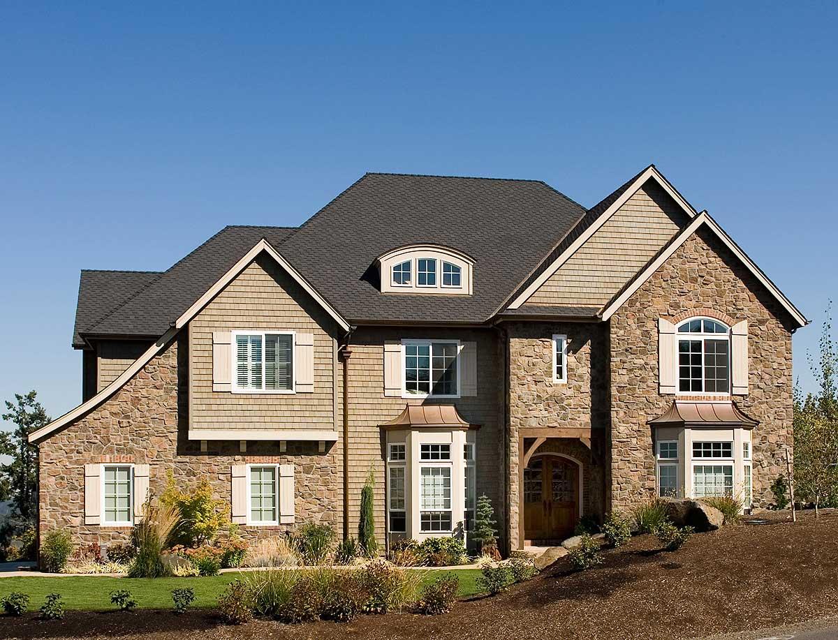 House plan exterior with stone and shake siding, a steeply pitched roof, arched dormer, and a prominent entry with a wooden beam.