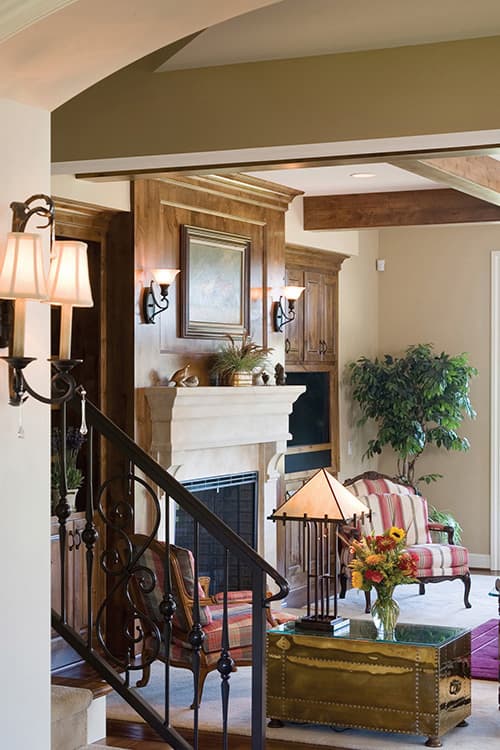 Interior view showing a stone fireplace with wood paneling, exposed beams, and a wrought-iron staircase.