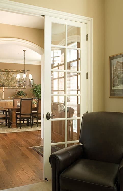 Open doorway with glass paneled French doors leads to a dining room with a table, chairs, and chandelier.