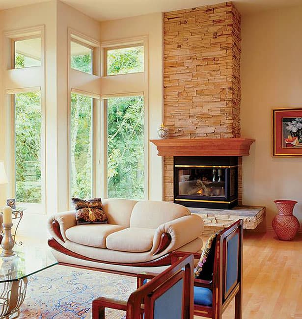 Living room interior with a stacked stone fireplace, sectional windows, and natural wood trim.