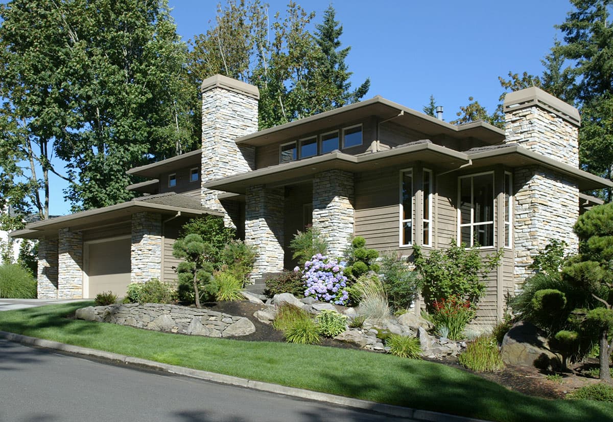 Modern house plan exterior with stone accents, overhanging eaves, large windows, stone chimney, and a side-entry garage.