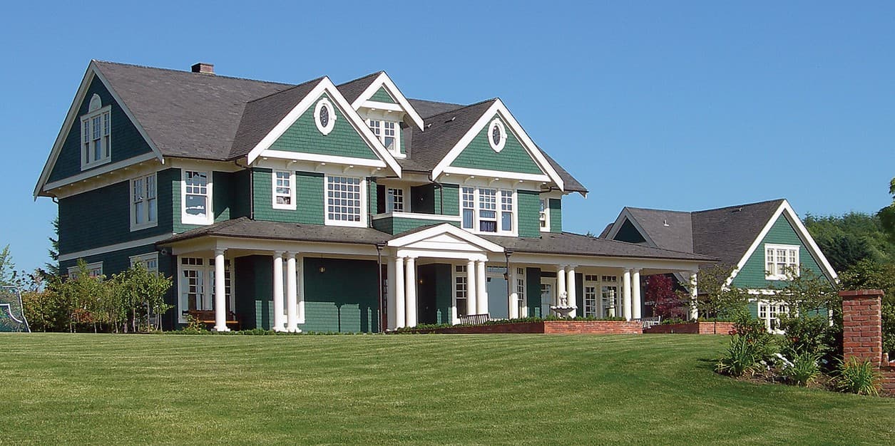 Craftsman style house plan exterior with multiple gables, dormers, wraparound porch supported by columns, and decorative window surrounds.