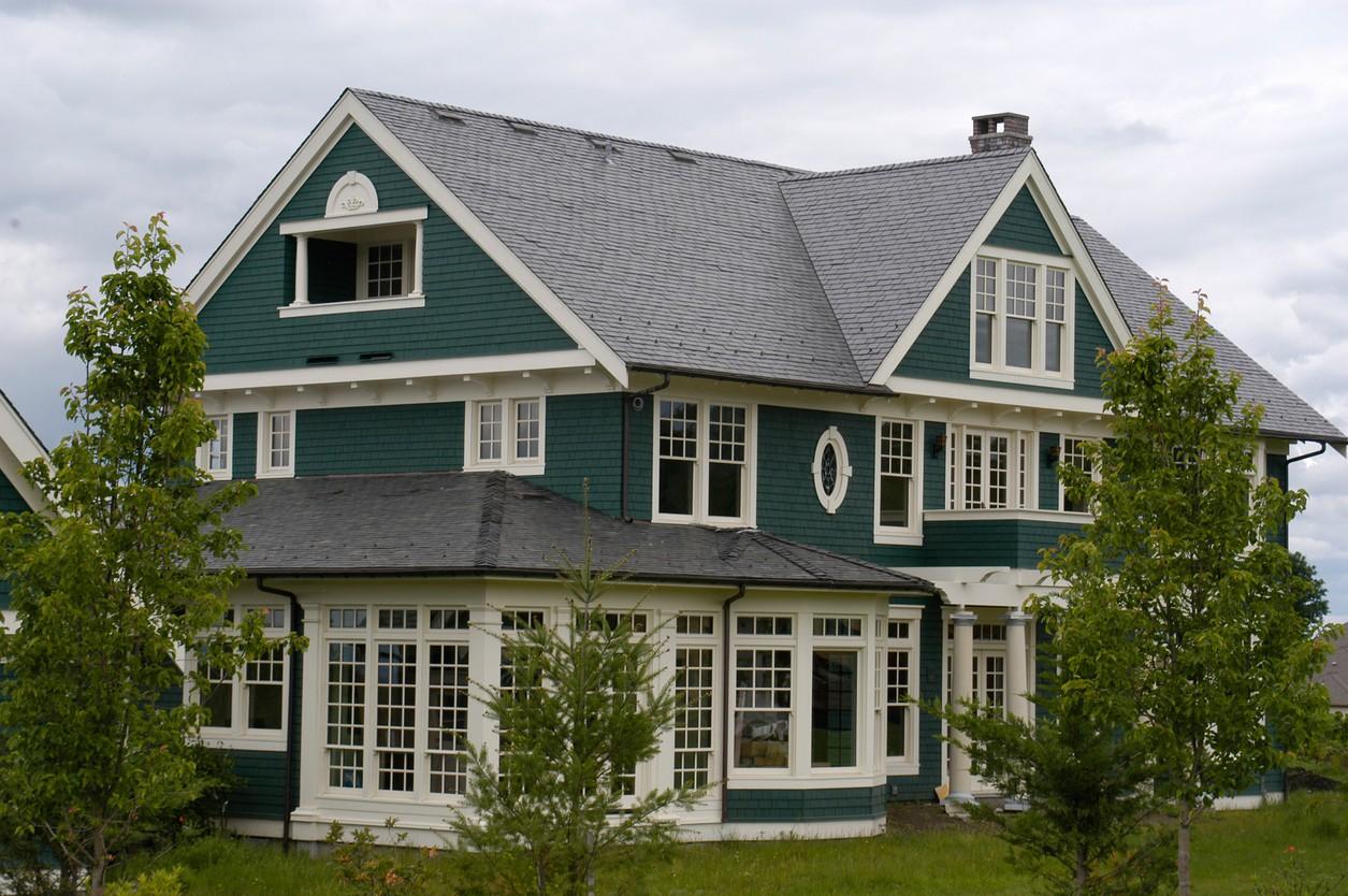 House plan exterior of a two-story home with dark green siding, prominent gables, dormers, and a sunroom with large windows.