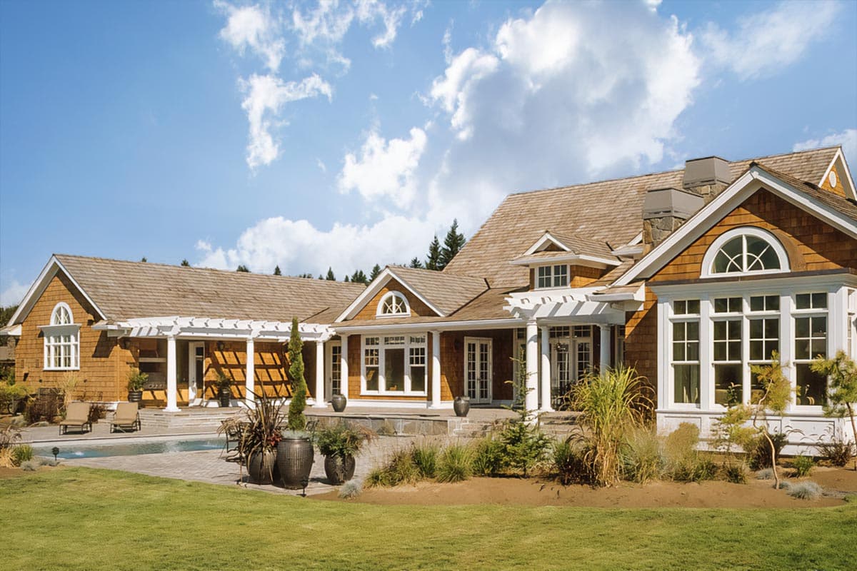 Craftsman style house plan exterior with wood shake siding, multiple gables, and a covered pergola leading to French doors.