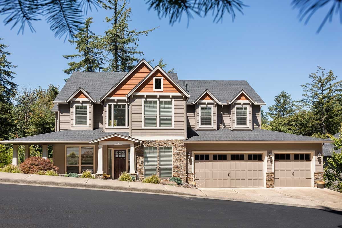 House plan exterior: Two-story home with wraparound porch, stone accents, dormers, and a three-car garage.