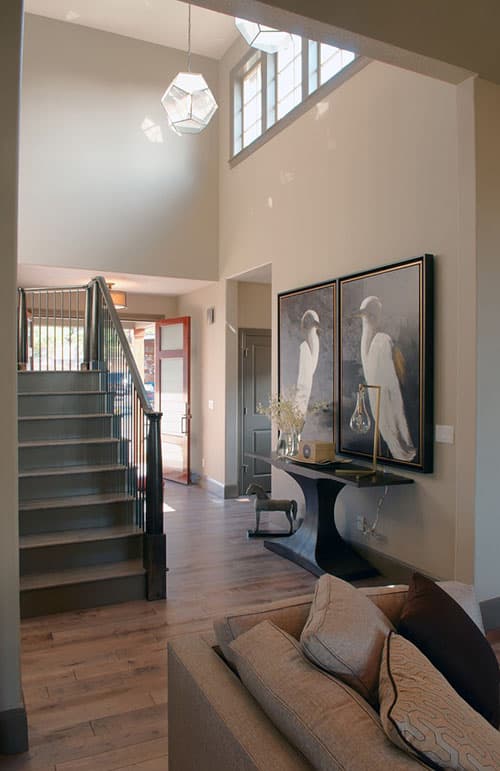 Interior view of a two-story entryway with a floating staircase, high ceiling with clerestory windows, and modern pendant light.
