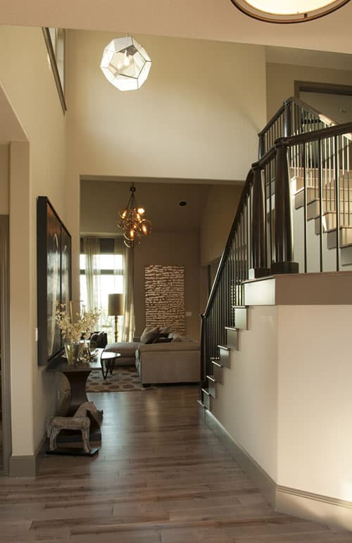 Interior view of a house entrance with open staircase, chandelier, and view into living room with sectional sofa.