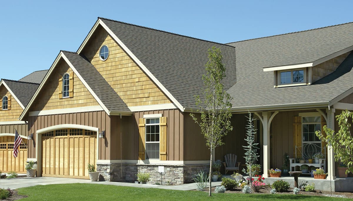 House plan exterior: Modern Farmhouse style, two-story home with gable dormers, cedar shake siding, stone foundation, and arched garage doors.